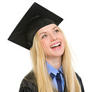Portrait of smiling young woman in graduation gown looking on co