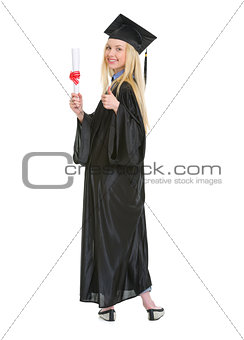 Full length portrait of young woman in graduation gown showing d