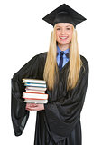 Portrait of smiling young woman in graduation gown holding books
