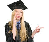 Young woman in graduation gown pointing on copy space