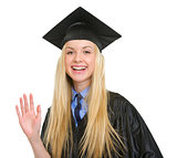Happy young woman in graduation gown greeting