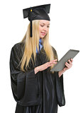 Happy young woman in graduation gown using tablet pc