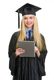 Smiling young woman in graduation gown using tablet pc