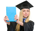 Young woman in graduation gown showing book