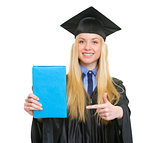 Young woman in graduation gown pointing book