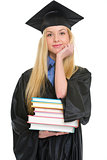 Happy young woman in graduation gown with books