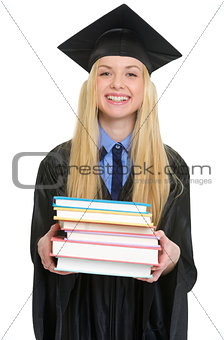 Happy young woman in graduation gown giving books