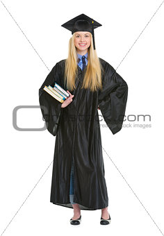Full length portrait of young woman in graduation gown with book