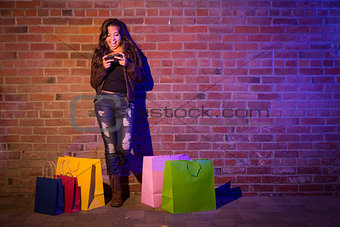 Woman with Shopping Bags Using Cell Phone Against Brick Wall