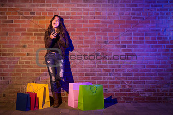 Woman with Shopping Bags Using Cell Phone Against Brick Wall