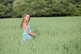 Beautiful teenager girl walking on a green oat meadow