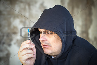 Drug addict men looks at the syringe in the hands