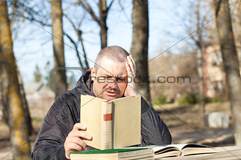 Man reading a book outdoors on a bench in the park