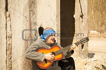 Man playing guitar leaning against wall
