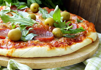 Pepperoni pizza with tomato sauce and herbs on a wooden board