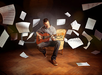 Young man playing guitar with sheet music flying around him