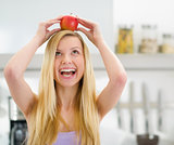 Happy teenager girl with apple on head in modern kitchen