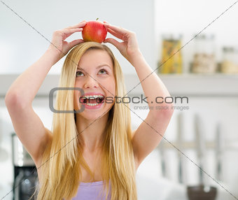 Happy teenager girl with apple on head in modern kitchen