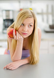Thoughtful teenager girl with apple in kitchen