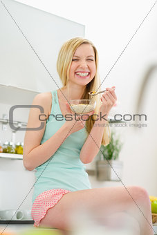 Smiling teenager girl sitting in kitchen and eating flakes with 