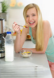 Smiling teenager girl having breakfast eating flakes with milk