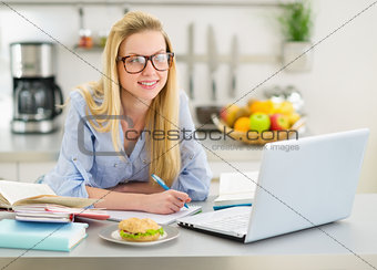 Happy teenager girl studying in kitchen