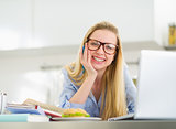 Happy young woman studying in kitchen