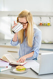 Young woman drinking coffee while studying in kitchen