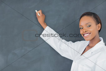 Teacher writing on a blackboard while looking at camera