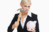 Stern businesswoman holding a hammer and a piggy-bank