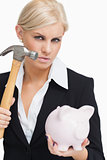 Beautiful businesswoman holding a hammer and a piggy-bank