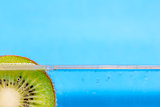Closeup of a kiwi slice floating in sparkling water against an aqua blue background