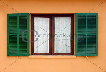opened green window shutters on yellow house facade