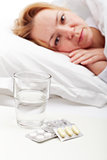Woman laying sick with pills and glass of water