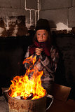 Poor beggar child warming up at the fire in a tin pot