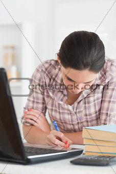 Woman writing on a notebook next to laptop