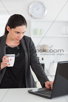 Woman looking at a laptop while holding a mug