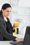 Woman using a laptop while holding a juice glass