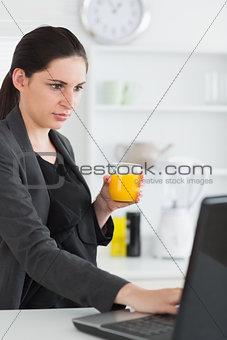 Woman using a laptop while holding a juice glass
