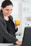 Woman holding a juice glass while looking at a laptop