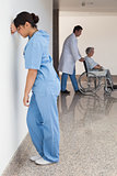 Distressed nurse standing against wall