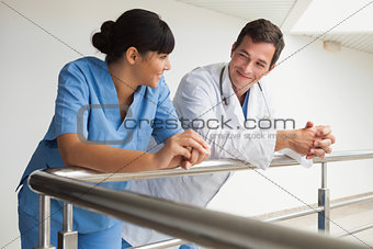 Doctor and nurse smiling and leaning against rail