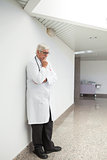 Thinking doctor leaning against wall