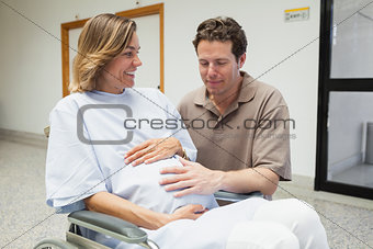 Pregnant woman and partner both touching her belly and smiling
