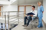 Doctor sitting in wheelchair examining notes with nurse