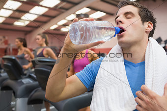 Man drinking water in the gym with towel around neck