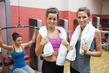 Two women with towels with woman using weight machine