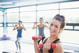 Smiling woman lifting weights while women doing aerobics