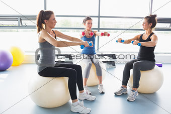 Three women lifting weights together on exercise balls