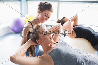 Female trainer helping woman doing sit-ups